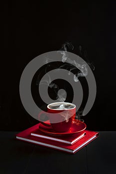 A red cup with fragrant coffee on a black background. Two red notebooks. Business style. The concept of a business