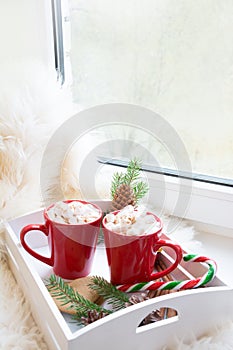 Red cup of hot chocolate with marshmallow on windowsill. Weekend concept. Home style. Christmas morning.