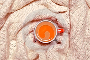 Red cup of hot sea buckthorn tea on backdrop from white knitted sweater on a rustic wooden background. Immunization concept. Top