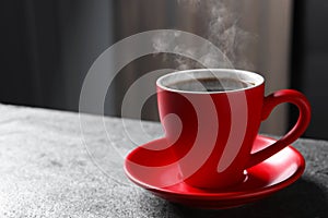 Red cup with hot steaming coffee on grey table indoors, space for text