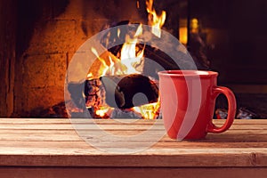 Red cup over fireplace on wooden table. Winter and Christmas holiday concept