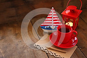 Red cup of tea and letter paper next to vintage decorative boat and lantern on wooden old table. retro filtered image