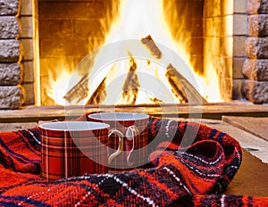 Red cups for hot tea and cozy warm scarf near fireplace.