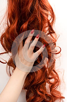 Red curly hair in woman hands with red nails