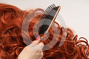 Red curly hair in woman hands with red nails