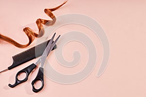 Red curly lock of hair, scissors and a comb on beige background