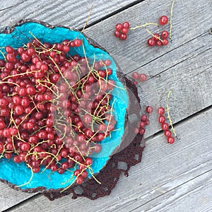 Red currant berry in a blue plate on a gray wooden background, top view , square format of photo