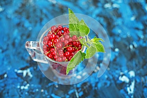 Red currant with mint on a blue background. Top view. The concept is healthy food, vitamins, diet and vegetarianism.