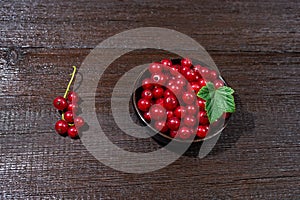 Red currants with leaves in a black bowl on a wooden background. Harvest of ripe summer berries. Closeup