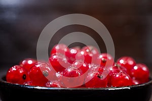 Red currants with leaves in a black bowl on a wooden background. Harvest of ripe summer berries. Closeup