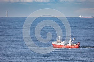 A red cutter on the North sea with a cargo ship and a wind turbine in the background