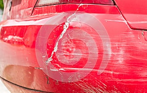 Red damaged car in crash accident with scratched paint and dented rear bumper metal body