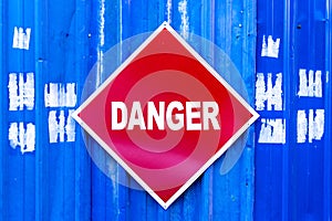 A red Danger sign mounted to a blue metal wall.