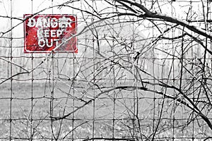 Red Danger sign posted to barbed fence tangled in branches, warn