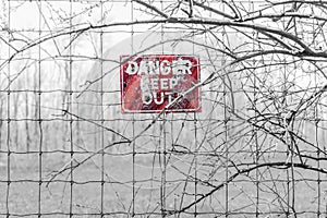 Red Danger sign posted to barbed fence tangled in branches, warn