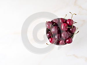 red dark sweet cherries in white bowl on stone white table, top view, copy space