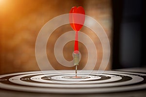 Red dart arrow hitting in the target center of dartboard on bullseye