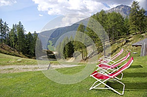 Red deckchairs to rest hikers and admire the high mountains with meadows, woods and rocks