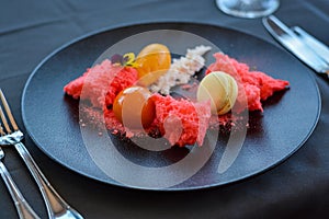 Red desert with macaron on black plate in restaurant.