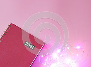Red diary or planner 2021 with glowing string lights  on pink background. New year 2021 planning, Bright year concept