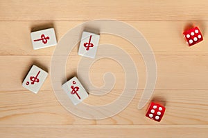 Red dice and bones tiles for mahjong on a light brown wooden background.