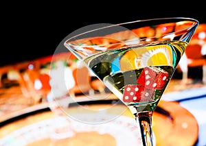 Red dice in the cocktail glass in front of roulette wheel
