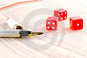 Red dice and golden pen on financial newspaper