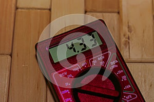Red digital measuring multimeter on wooden floor. It shows 4.33V or fully charged battery. Includes voltmeter, ampermeter, ohmmete