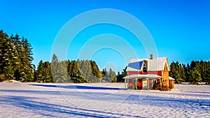 Red dilapidated and abandoned house in a wide snow covered field in Glen Valley in the Fraser Valley of British Columbia