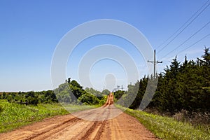 Red dirt road in the country with tire tracks leading up over horizon