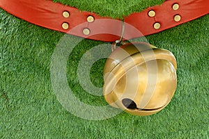 Red dog collar made from leather decorate with pins hanging big golden bell on green grass background with copy space