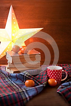 Red dotted Mug or tea cup with hot chocolate on a Scottish blanket. Cozy home concept with books. A Cup of festive hot