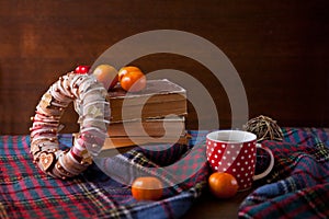 Red dotted Mug or tea cup with hot chocolate on a Scottish blanket with wreath. Cozy home concept with books. A Cup of