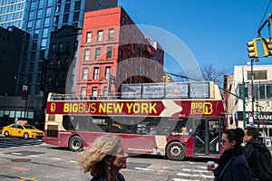 Red double decker tour bus is seen on a busy New York City street with tourists on the top level