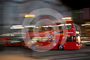 A red doubledeck London bus at night seen with motion blur against blurred lights