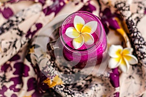 Red Dragon fruit juice in a glass, decorated with Plumeria flower over flowery fabric. Top view.