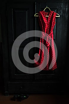 Red dress in a white dots on a wooden hanger on a black vintage wardrobe