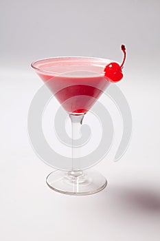 Red drink in martini glass, garnished with marachino cherry. on white background