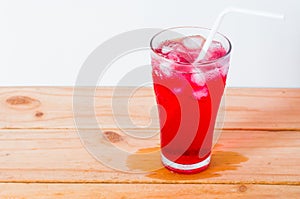 Red drinks with soda and ice with straw in glass on wooden background