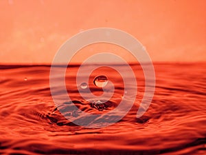 A red drop drips into the water and creates splashes of different shapes