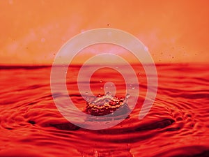 A red drop drips into the water and creates splashes of different shapes