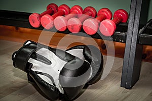 Red dumbbells for fitness and black and white boxing gloves on the floor