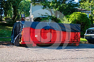 Red dumpster with black plastic liner on a asphalt street near the side of a house