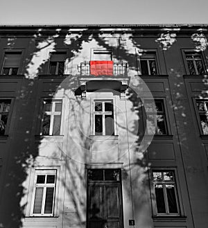 A red duvet draped over a balcony on the top floor of a house in black and white