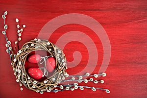 Red Easter background. Easter willow wreath with red Easter eggs on red background. Top view, copy space.