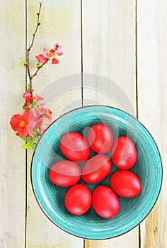 Red Easter egg on turquoise bowl and a small branch of flowering quince