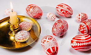 Red Easter eggs with folk white pattern on candlestick with burning candle in left side and eggs around on white background. Ukrai photo