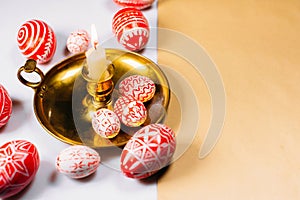 Red Easter eggs with folk white pattern on candlestick from left side on white beside paper for text.