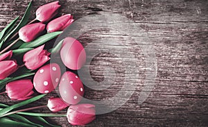 Red easter eggs and pink tulip flower on vintage wooden table from above