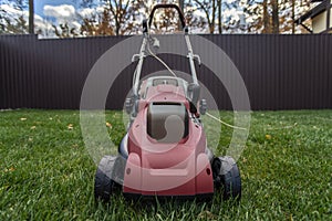 Red electric lawn mower on a green lawn.